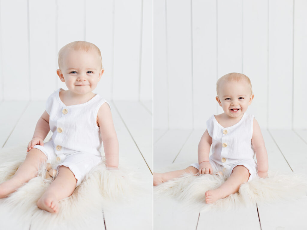 1 year old smiling baby boy in white romper with white wood background