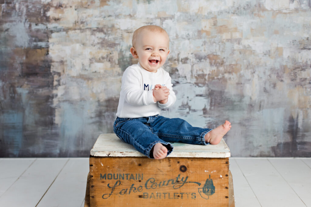 1 year old smiling baby boy in my first birthday shirt sitting on a wooden box