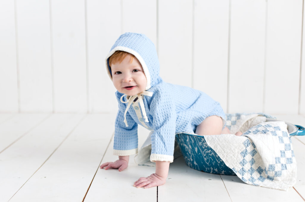 Baby boy sitter session with light blue romper and bonnet sitting in a bowl with a quilt piece.
