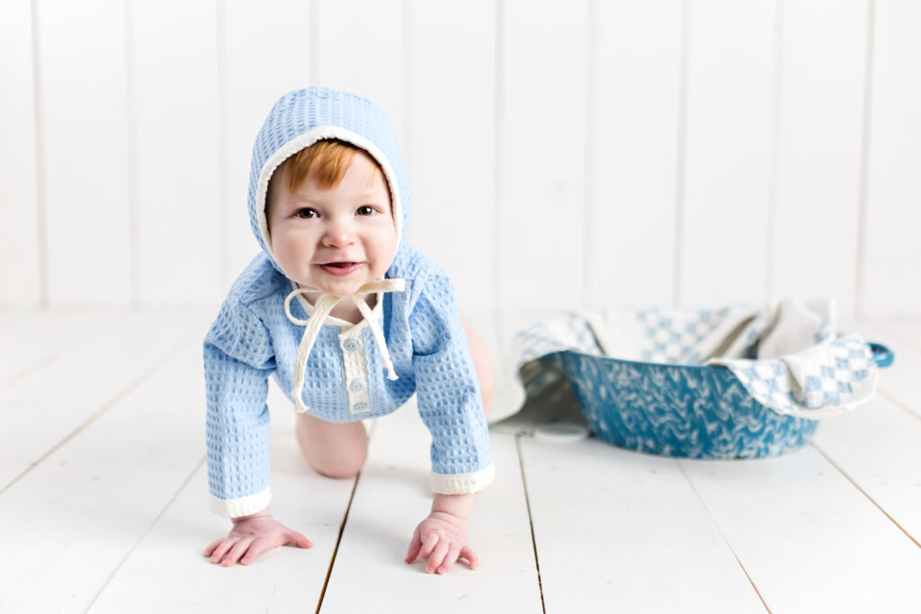 Baby boy sitter session with light blue romper and bonnet sitting in a bowl with a quilt piece.