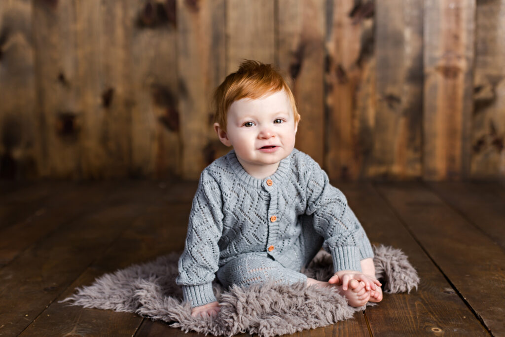 Baby boy sitter session with grey quilted romper on wood background.