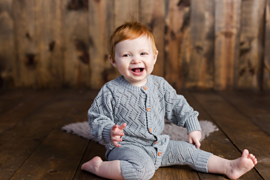 Baby boy sitter session with grey quilted romper on wood background.