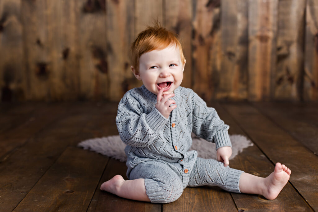 Baby boy sitter session with grey quilted romper on wood background.