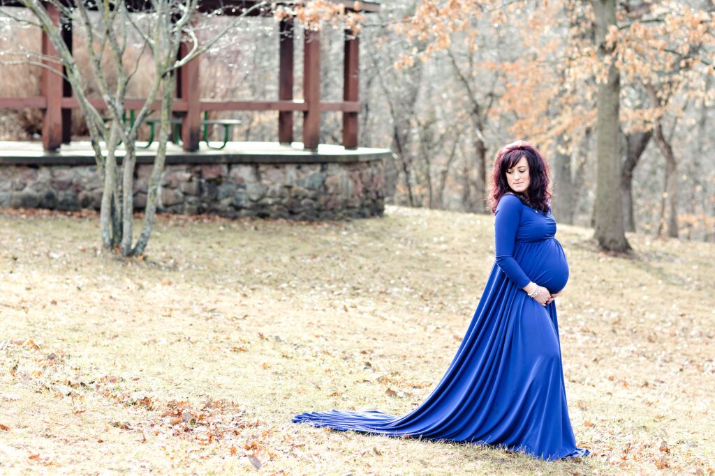 Maternity woman at a park in early spring Iowa wearing a blue flowing maternity gown.