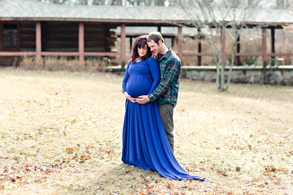 Maternity couple at a park in early spring Iowa wearing a blue flowing maternity gown.