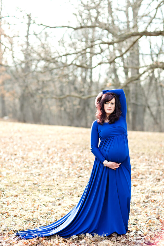 Maternity woman at a park in early spring Iowa wearing a blue flowing maternity gown.