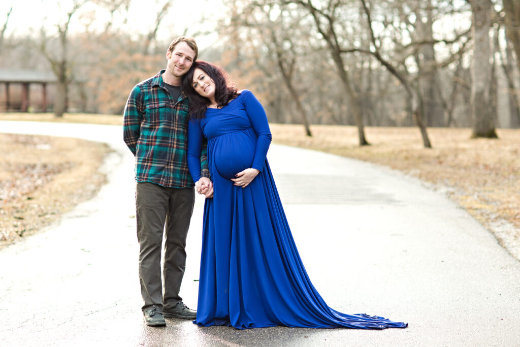 Maternity couple at a park in early spring Iowa wearing a blue flowing maternity gown.