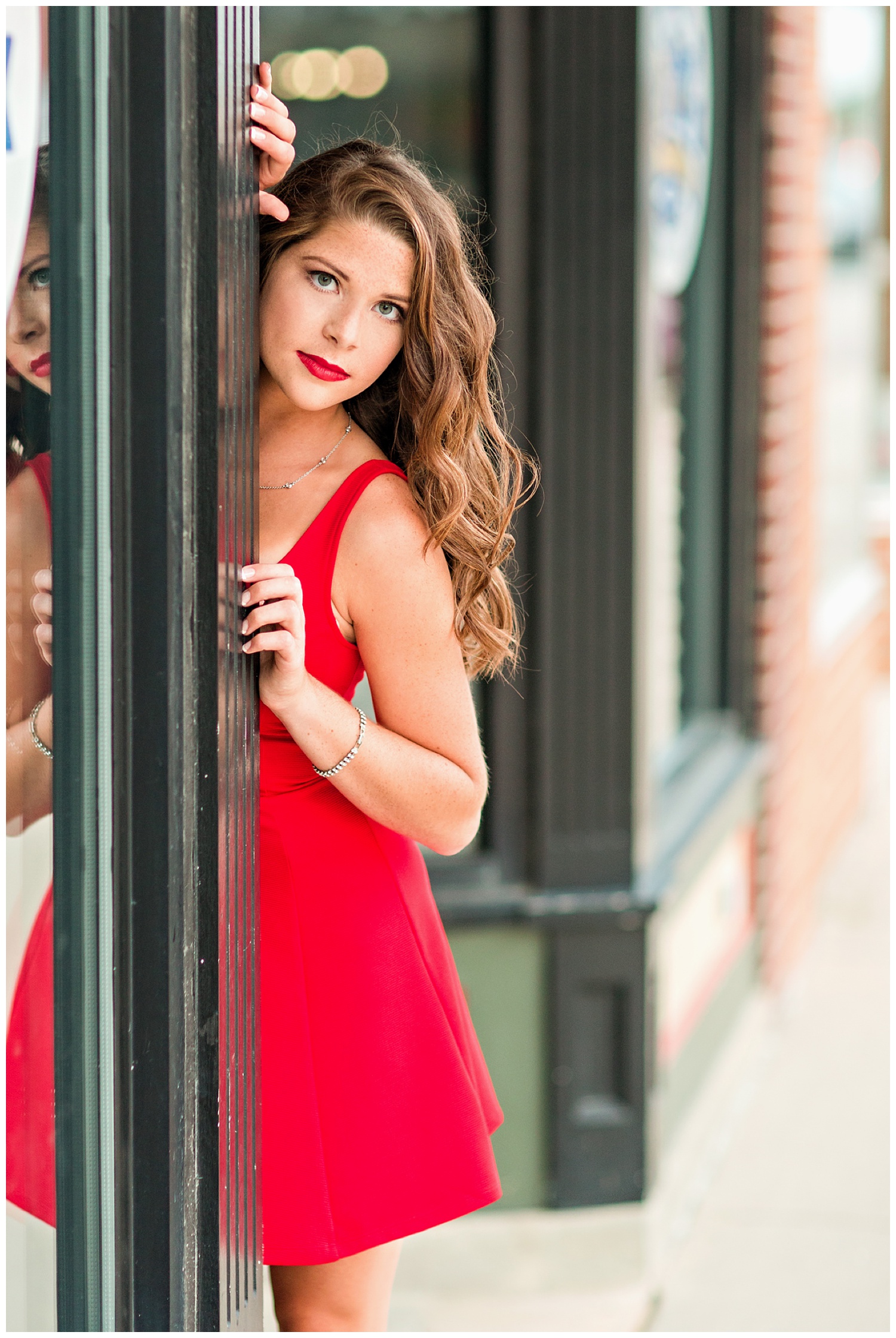Iowa senior girl wearing a red dress appearing from a door in downtown Algona, Iowa