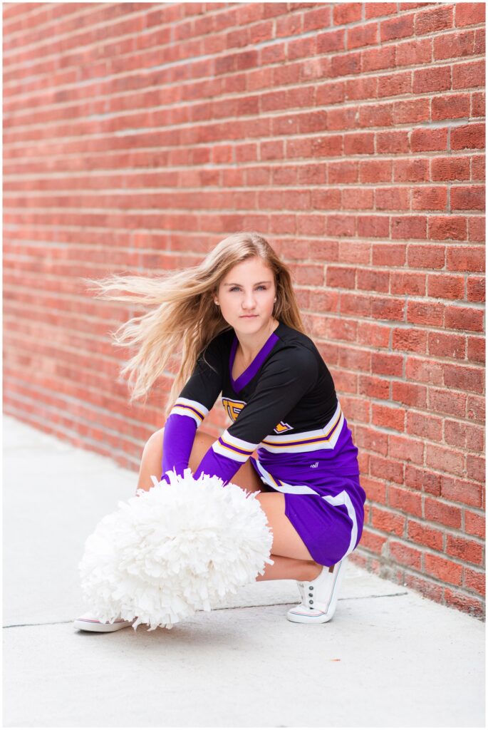 Senior girl portraits in dance/cheerleading uniform along a brick wall | Iowa Senior Photographer | CB Studio