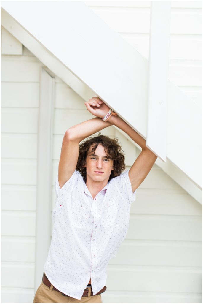 Senior boy poses standing under a white staircase in downtown Algona, IA CB Studio Photography