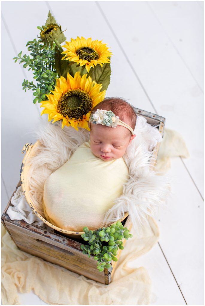 Newborn wrap posed in a yellow rustic bucket and box wearing a yellow wrap with sunflower, flotaki blanket and white details | Iowa Newborn Photographer | CB Studio