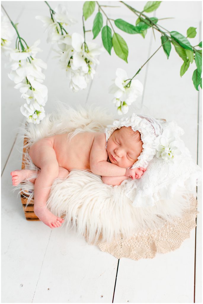 Newborn posed in a rustic box wearing a white lace bonnet with a lace pillow, flotaki blanket and white flower details | Iowa Newborn Photographer | CB Studio
