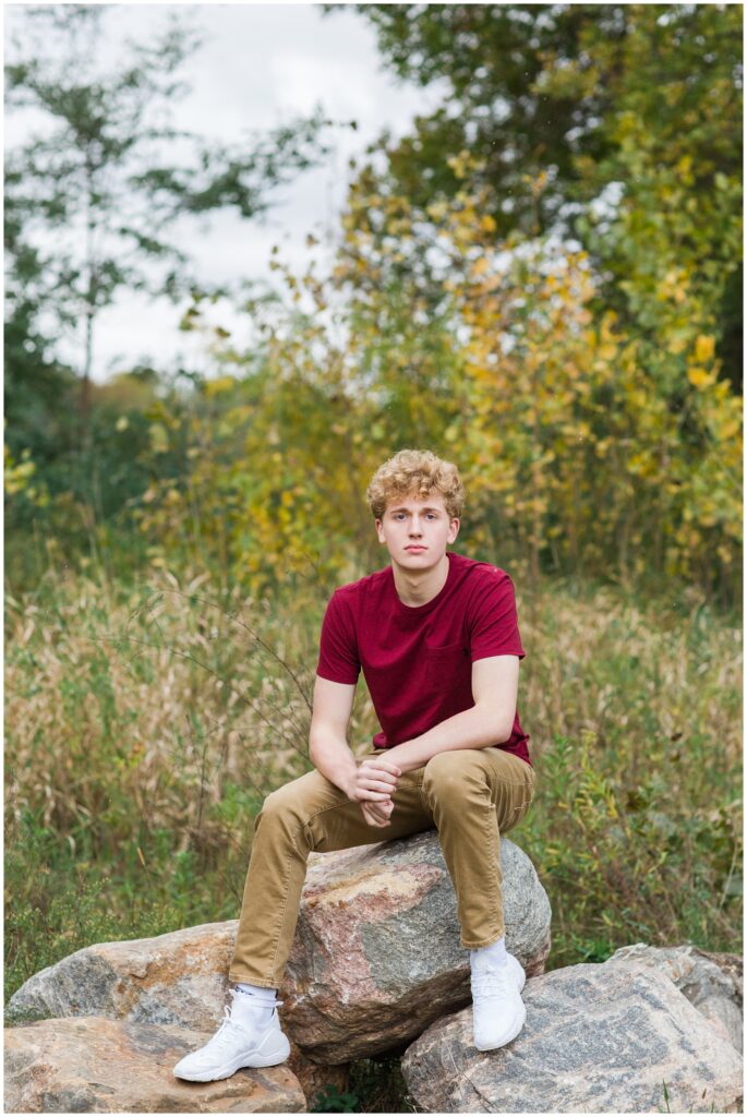Senior boy on some large rocks surrounded by fall foliage at Plum Creek Wildlife Area | Iowa Senior Photographer | CB Studio