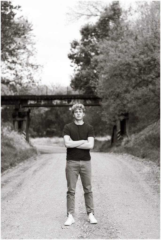 Senior boy standing on a gravel road in front of an old railroad bridge at Plum Creek Wildlife Area | Iowa Senior Photographer | CB Studio