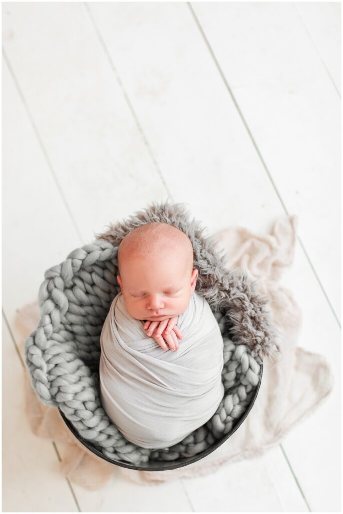 Newborn boy wrapped in gray and posed in a bucket on a white wood floor | Iowa Newborn Photographer | CB Studio