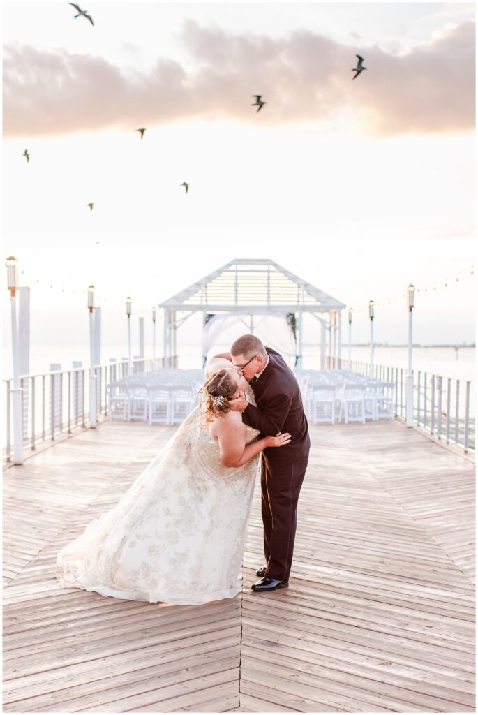 Bride and groom kissing on the pier of The Godfrey Hotel Tampa during sunset with seagulls flying over. | Tampa Bay Wedding | CB Studio