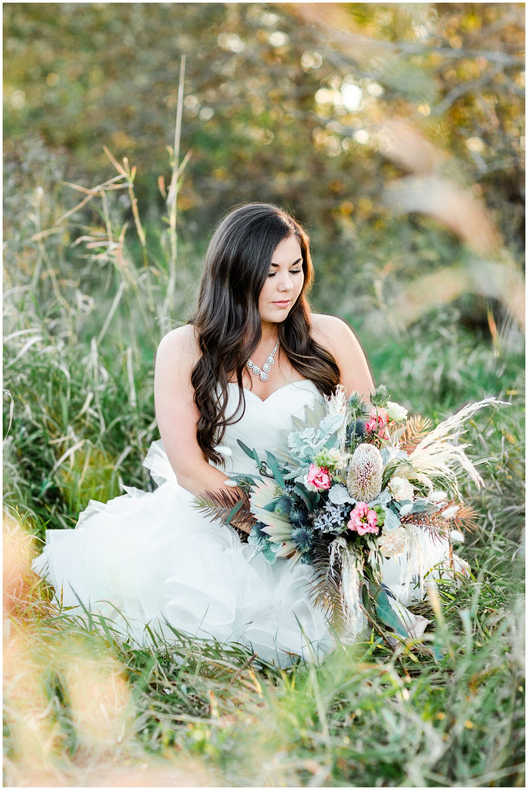 Bridal portrait sitting in a field with a large bouquet with soft florals