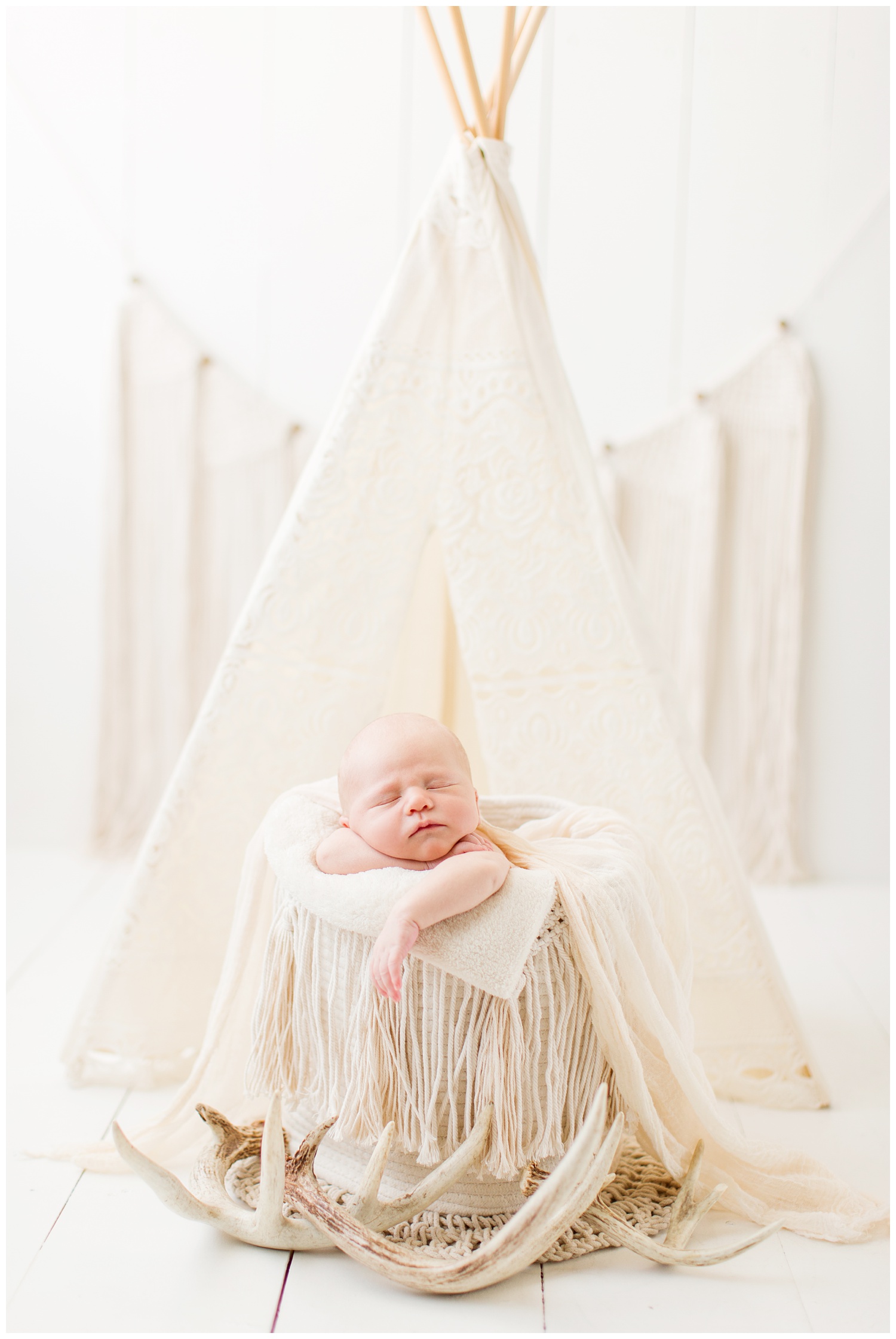 Newborn baby posing in a cream boho theme photography set up complete with deer antlers
