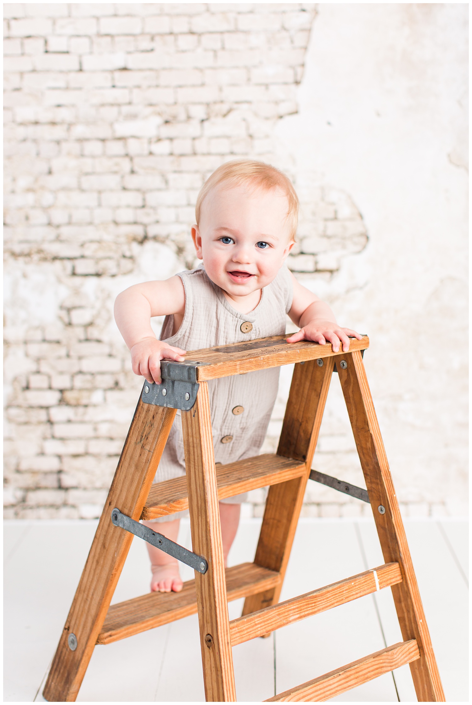 Baby Cullen poses on a wooden ladder in a gray vintage romper for his first birthday.