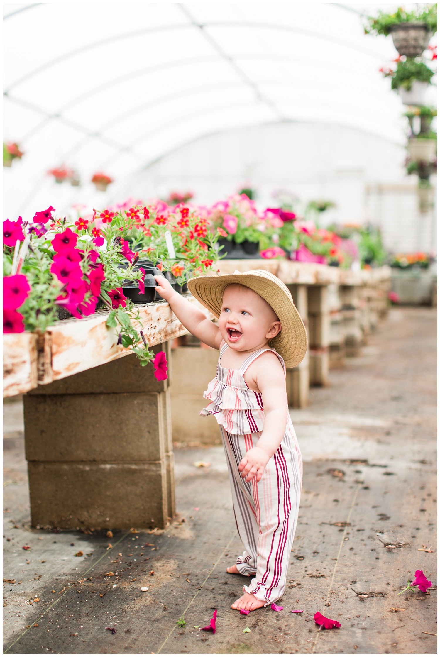 Baby Ivy standing along side florals in a greenhouse wearing a fun floppy hat.