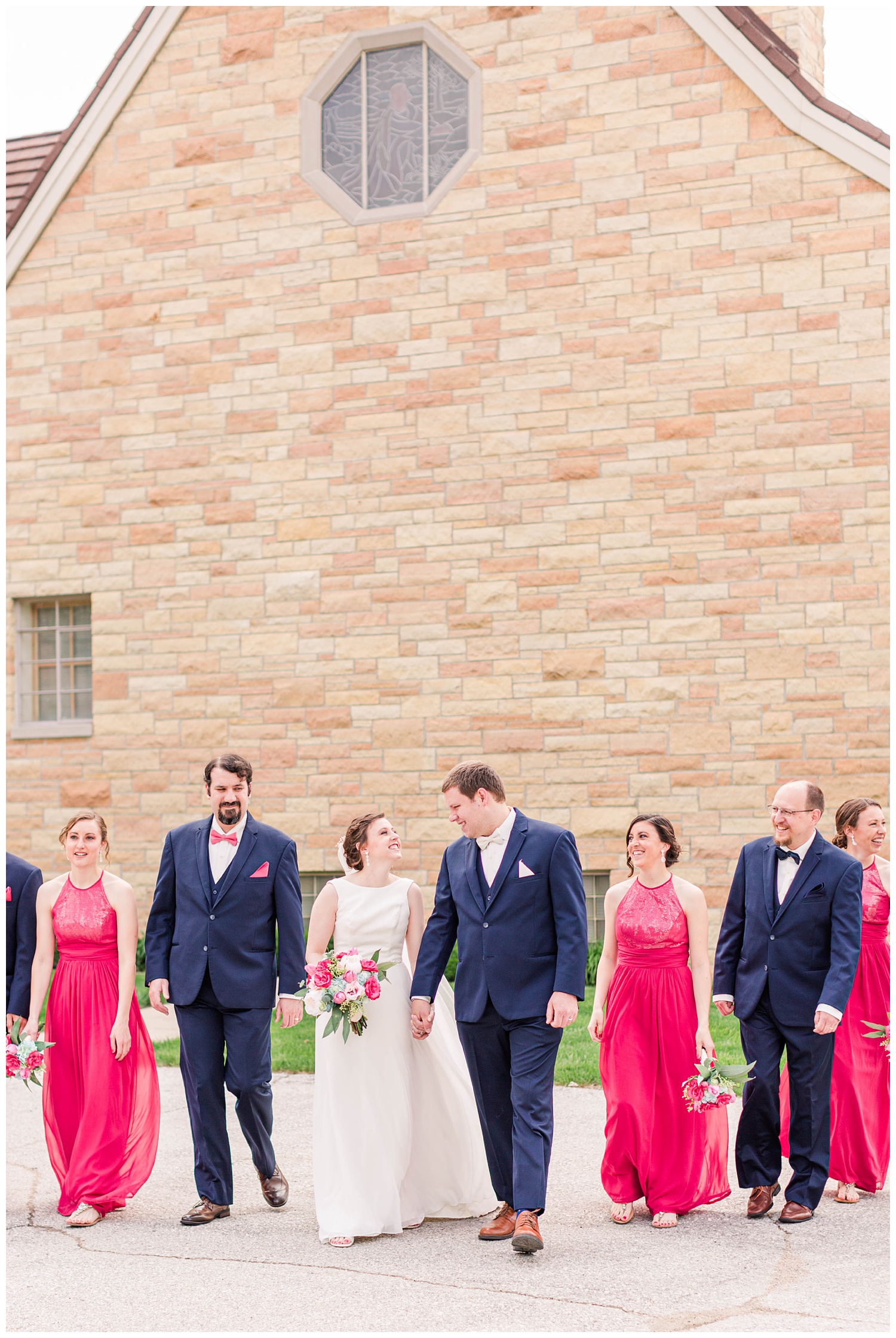 Wedding party wearing navy and Valentine pink walk away from a church in Algona Iowa | CB Studio