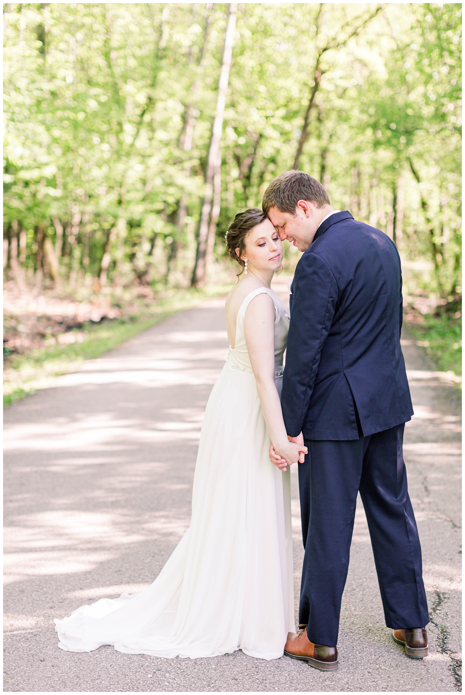 Bride and groom hold hands and nuzzle in close on a scenic path in Call Park Algona Iowa | CB Studio