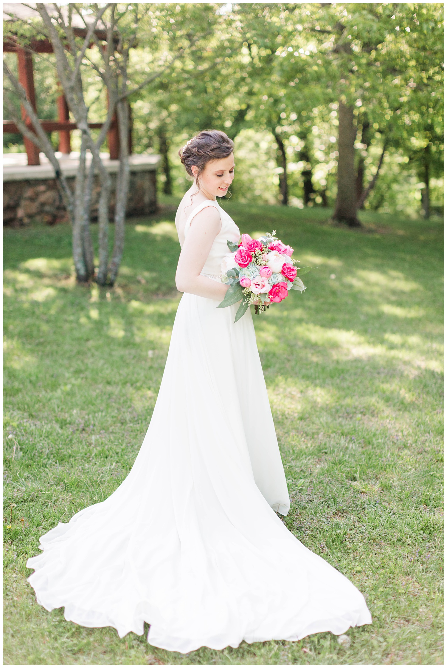 Bride wearing Justin Alexander holds white and deep pink bouquet in a scenic area of Call Park Algona Iowa | CB Studio