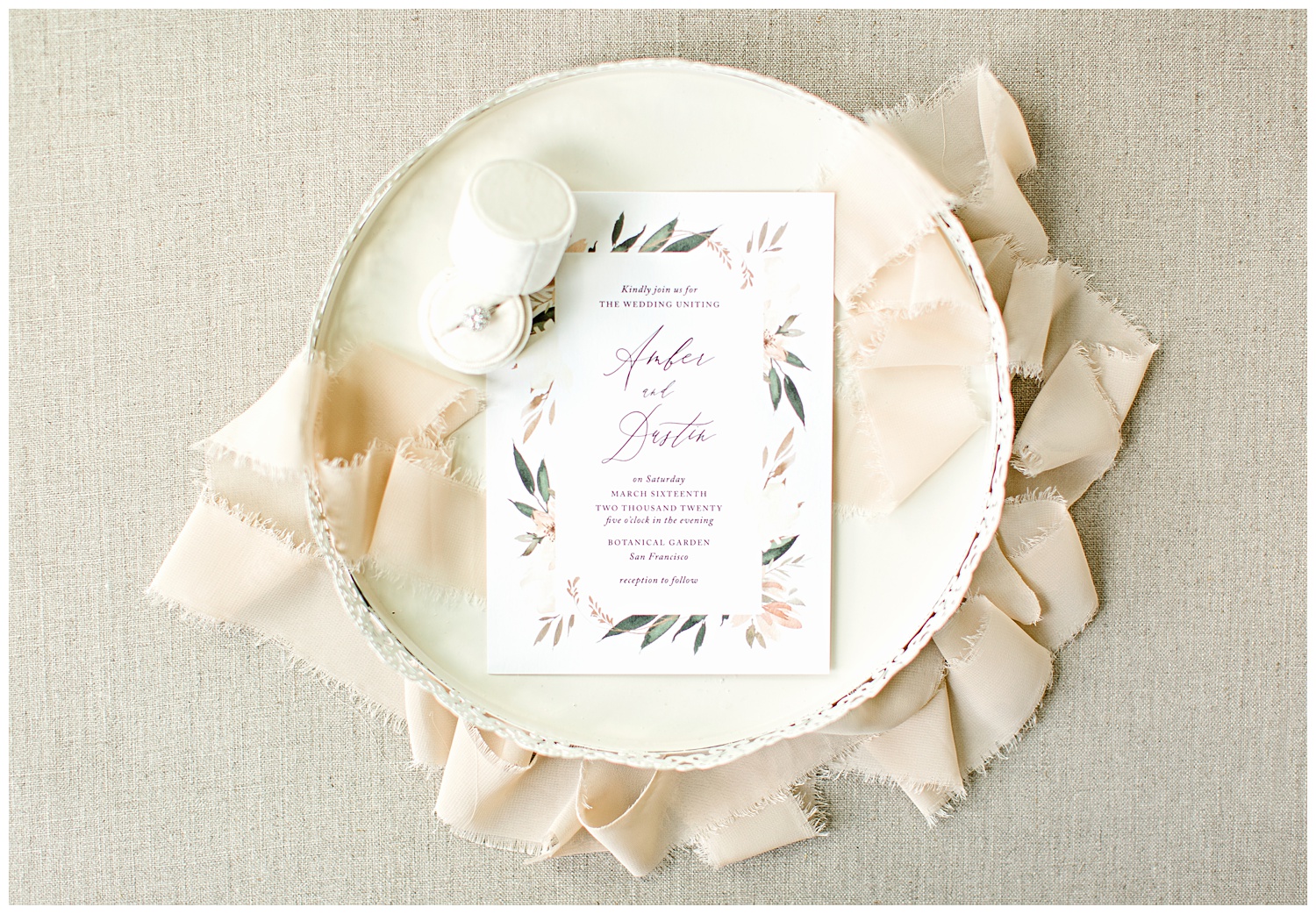 Peach and green watercolor floral wedding invitation from Elli beautifully styled on a cream decorative tray with a cream ring box and peach frayed edge ribbon.