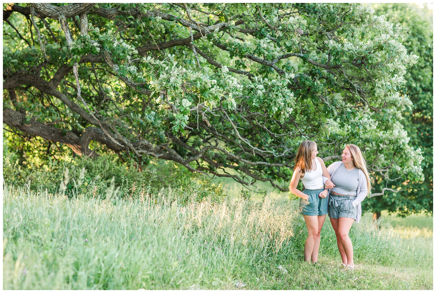 Senior girls best friends BFFs embrace laughing at each other in a grassy field on a rural Iowa farm | CB Studio