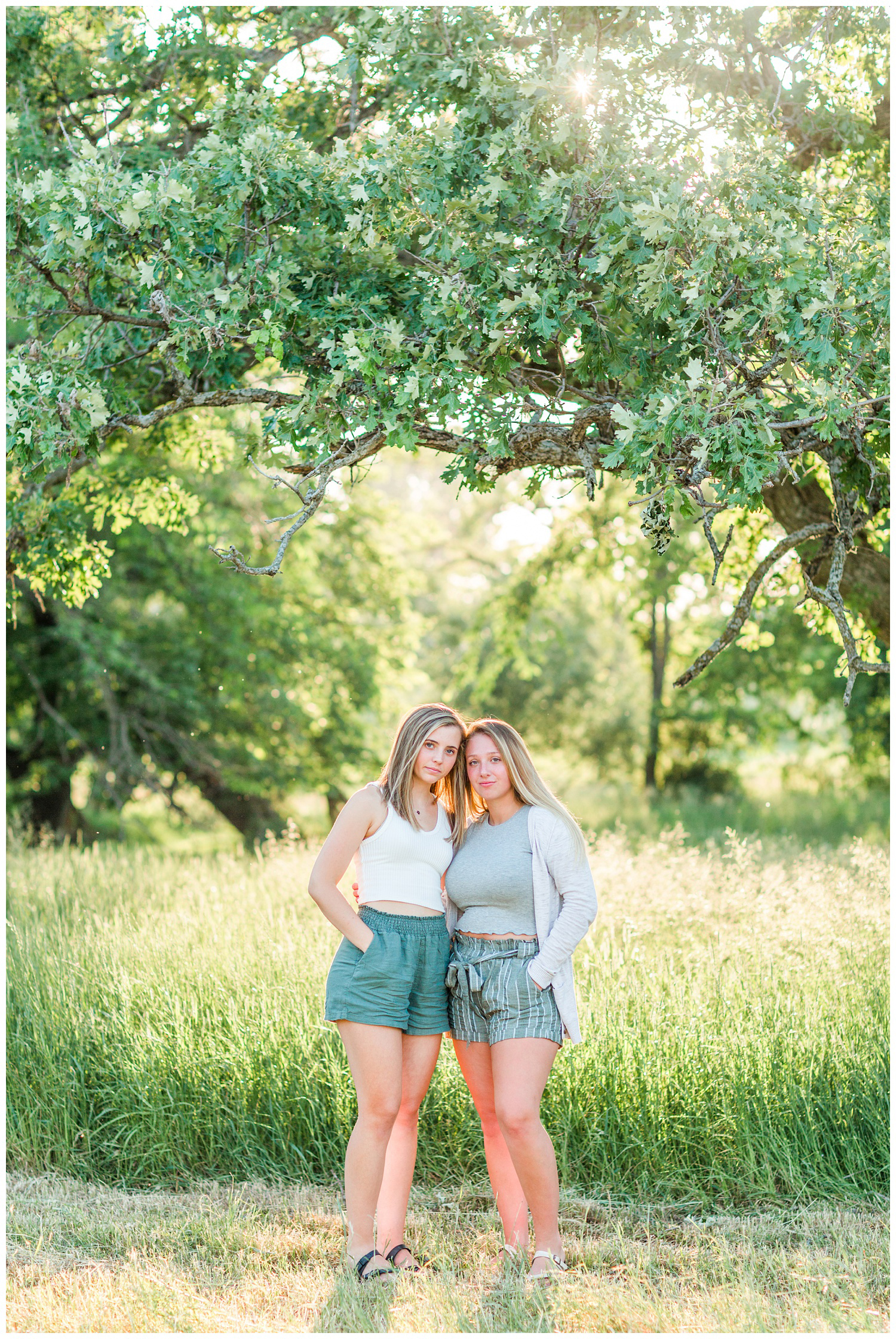 Senior girls best friends BFFs embrace in a grassy field on a rural Iowa farm with glowing, bright and airy lighting | CB Studio