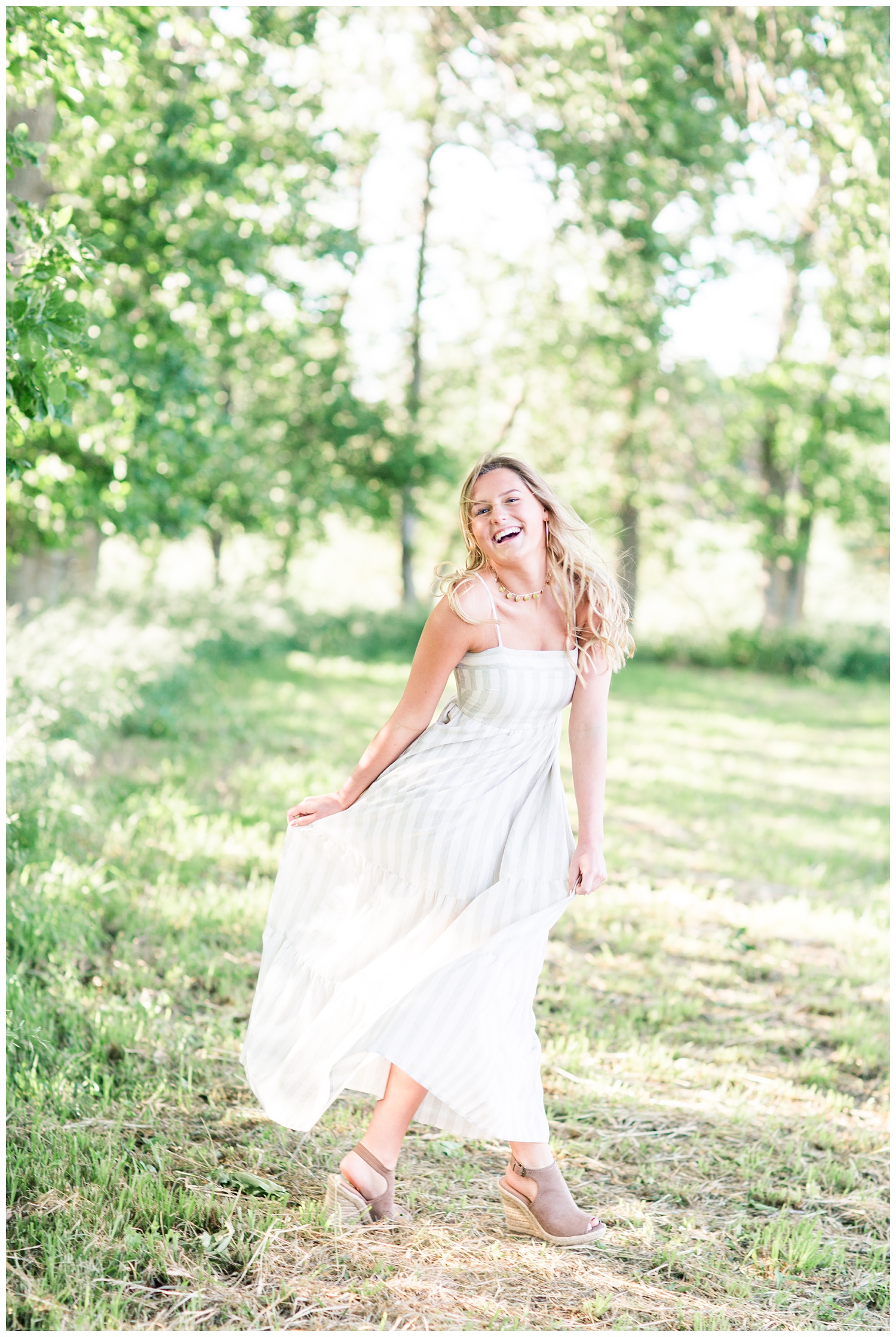 Senior girl dances in a grassy field wearing a flowing white summer dress | CB Studio