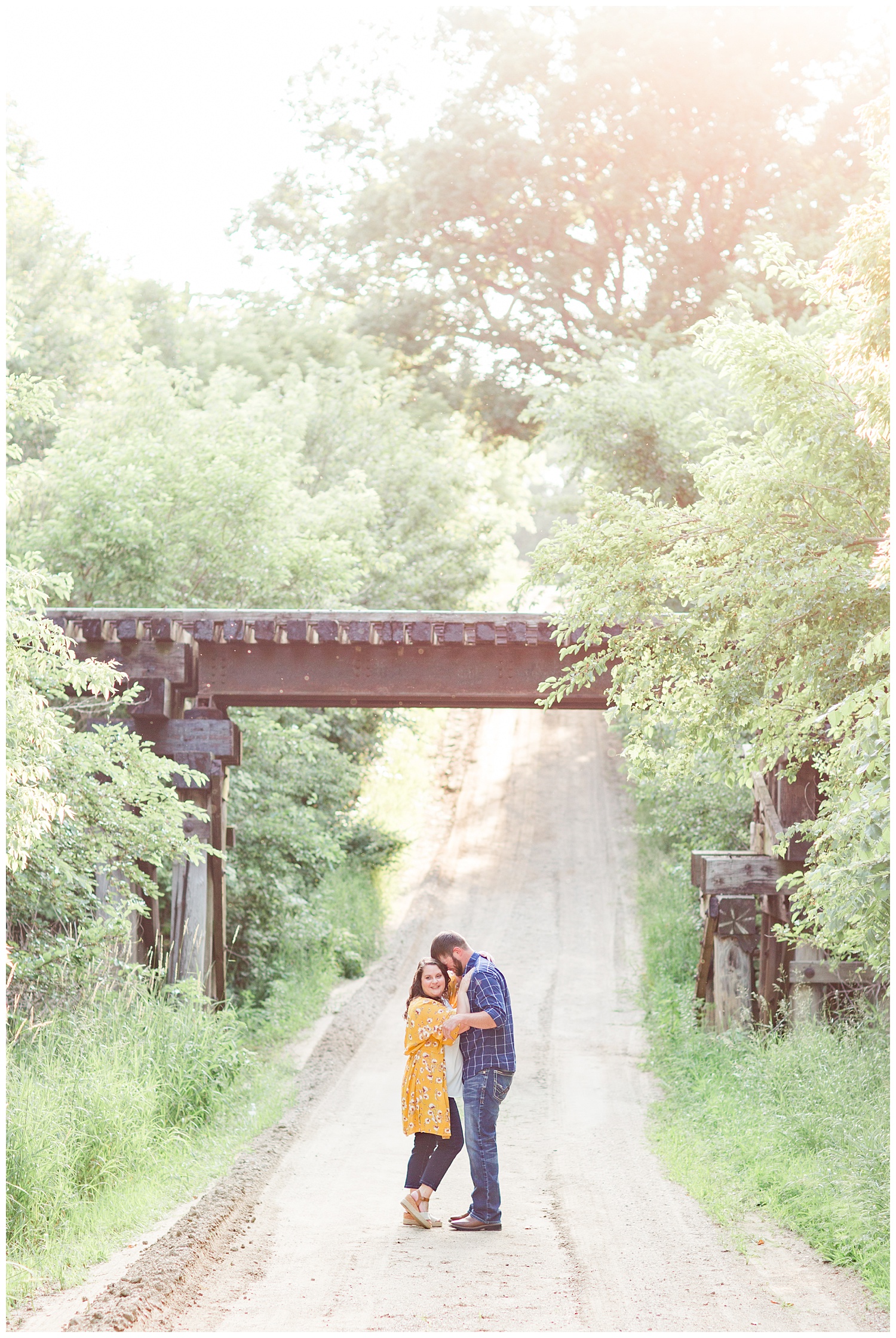 Engaged couple stands under a train trestle bridge on a farm in north central Iowa | CB Studio