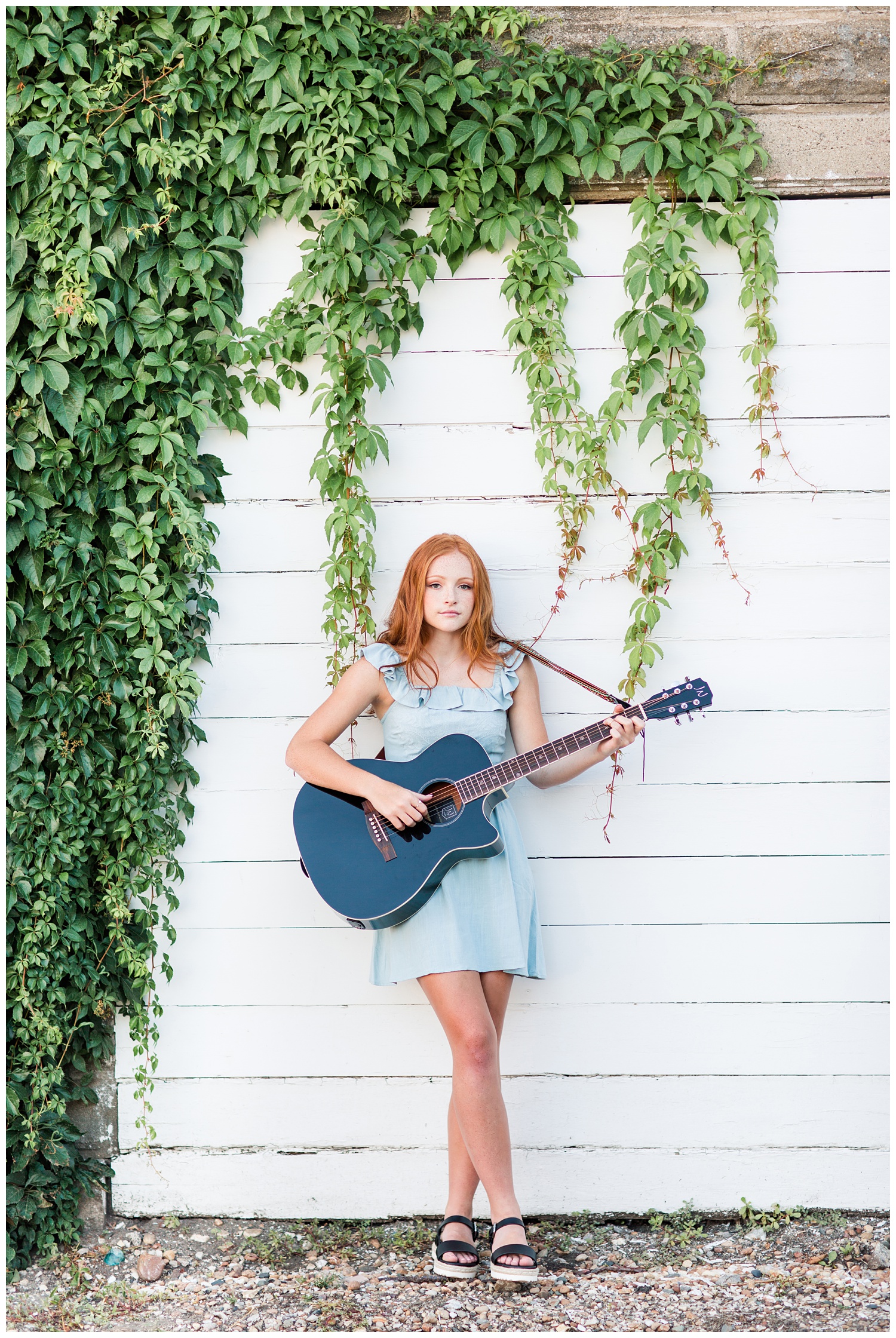 Senior girl leaning against a green vine wall playing guitar in West Bend, Iowa | CB Studio 