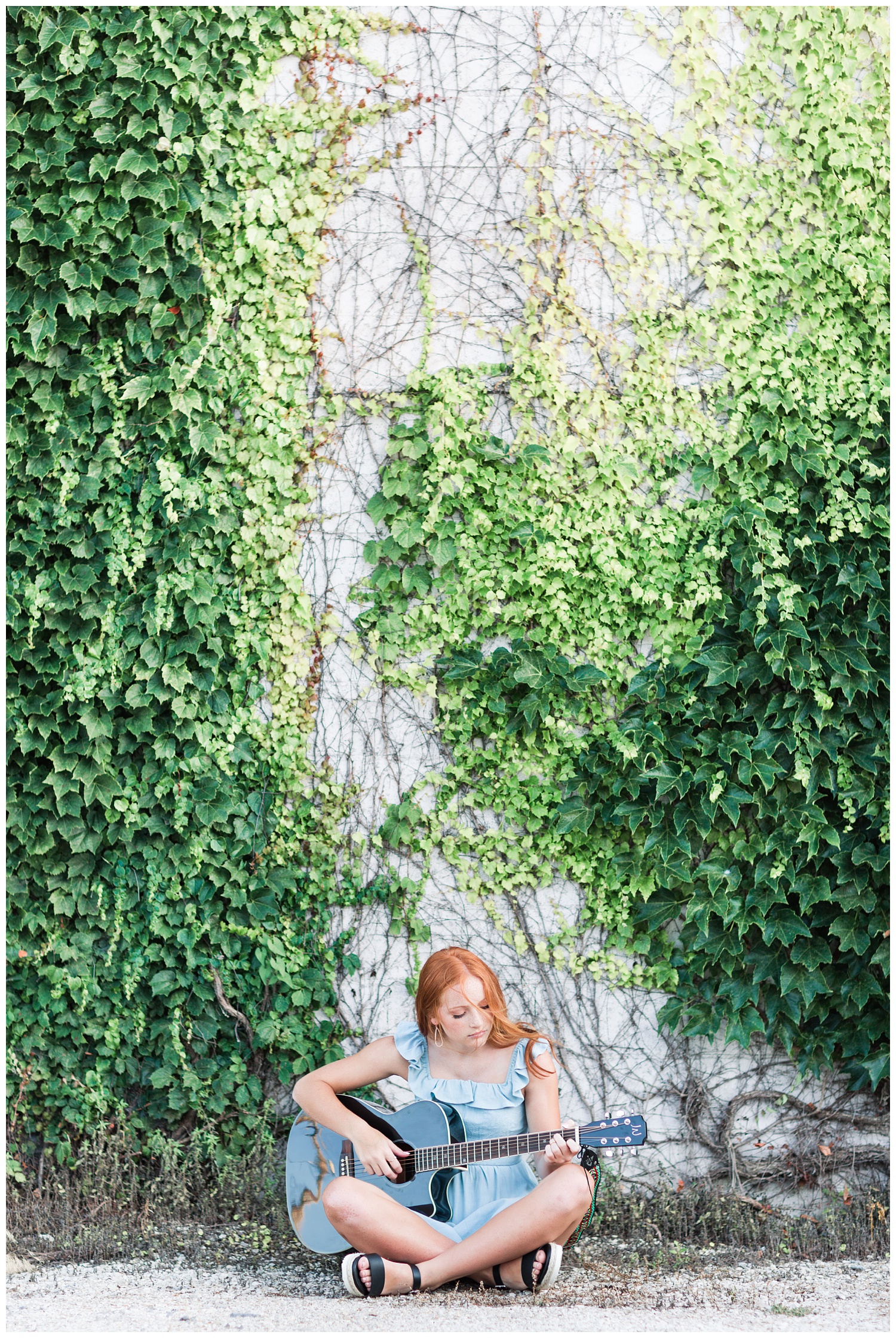 Senior girl sitting next to a green vine wall playing guitar in West Bend, Iowa | CB Studio 