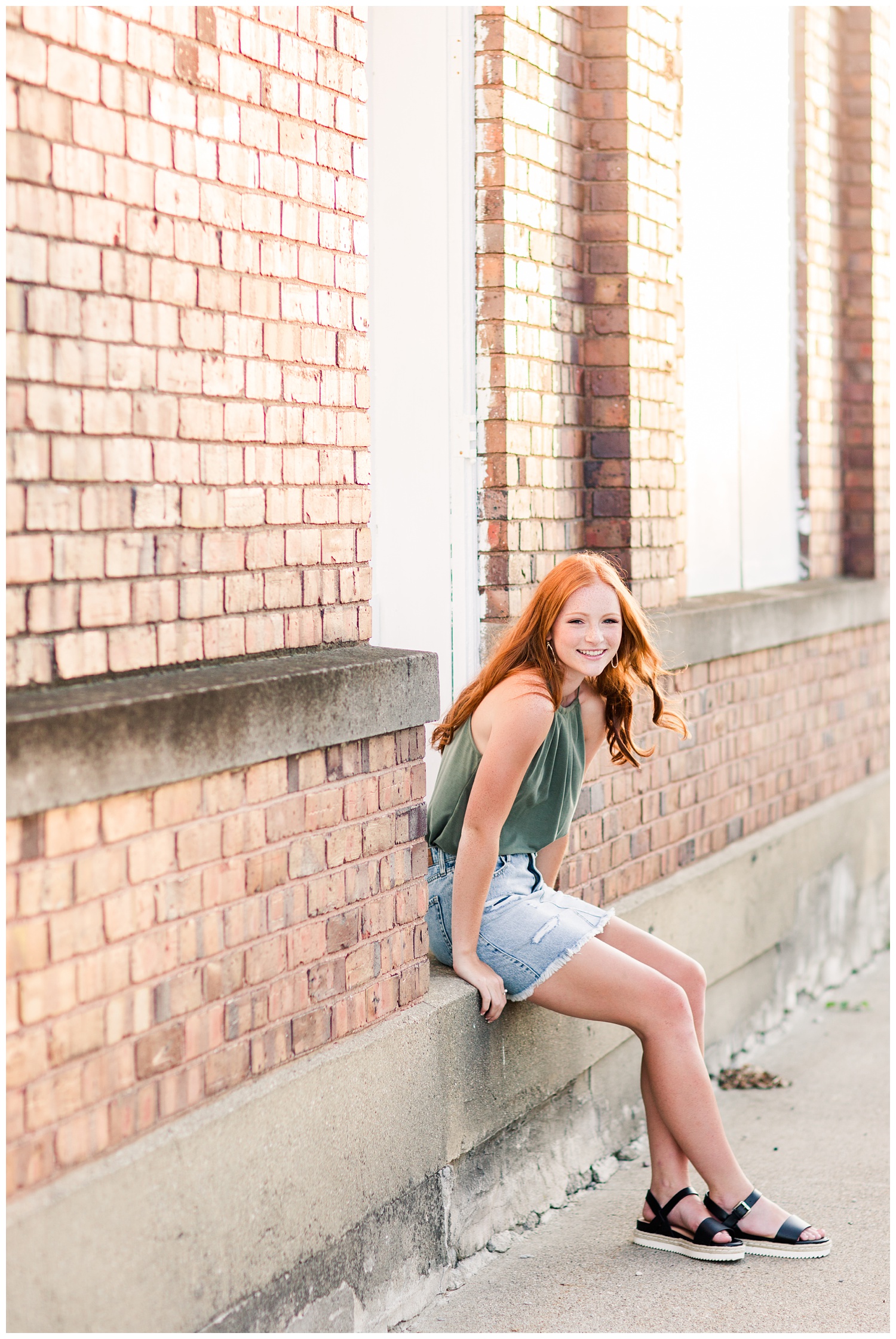 Senior girl sitting on a step next to a brick building during golden hour as the breeze blows through her hair in West Bend, Iowa | CB Studio 