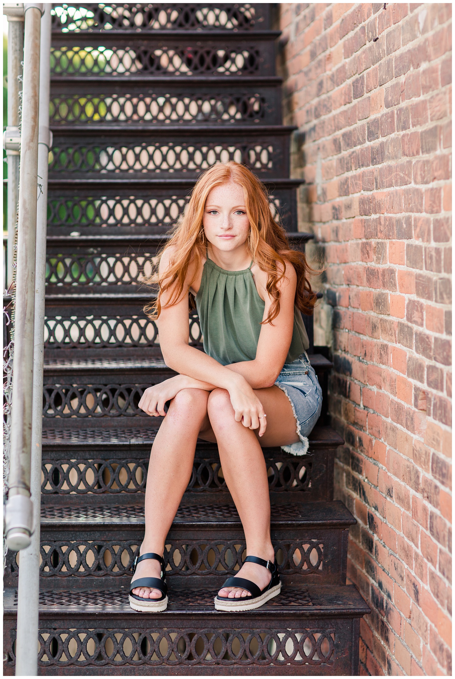 Senior girl sitting on an ornate wrought iron stair case as the breeze blows through her hair in West Bend, Iowa | CB Studio 