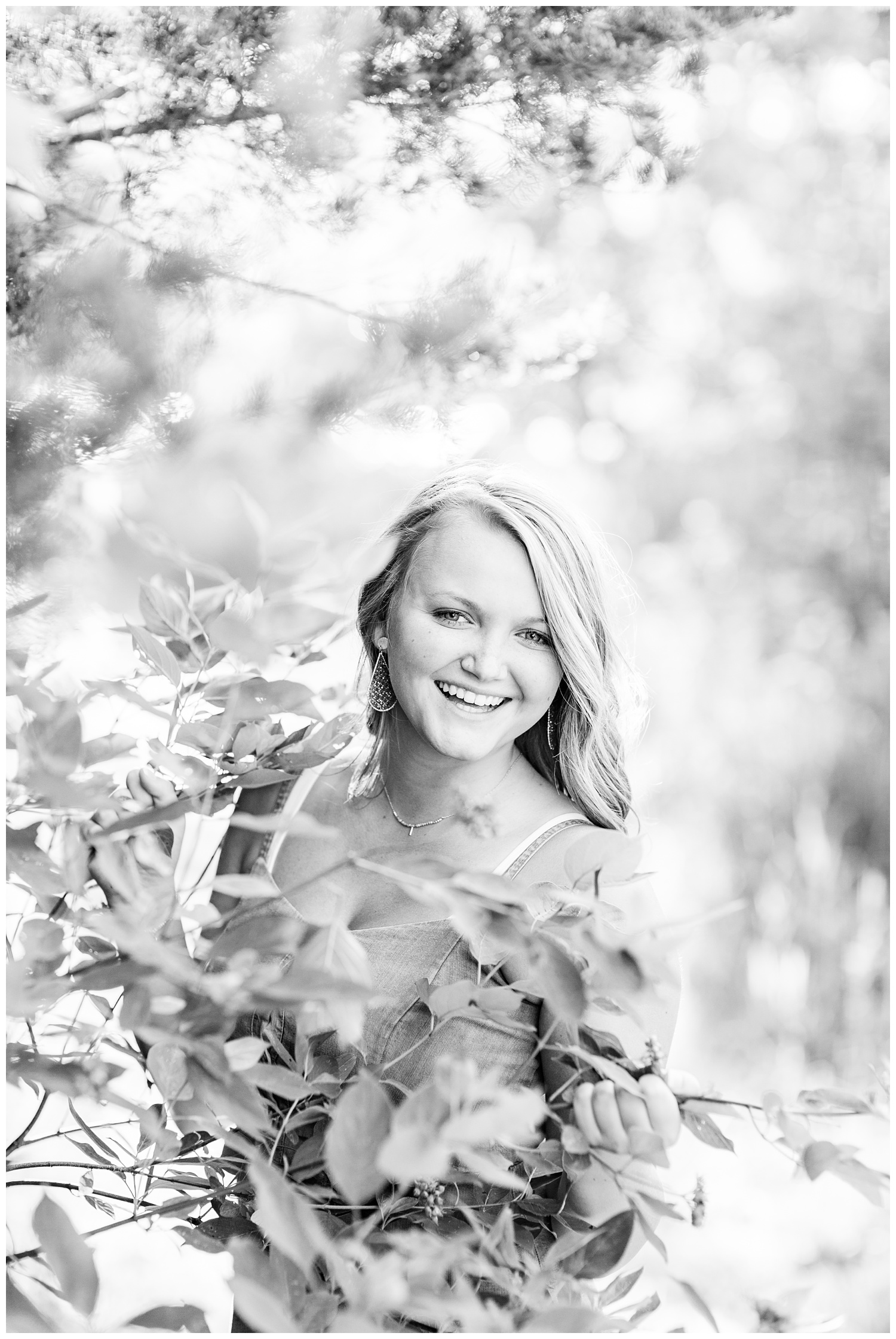 Senior girl wearing laughing behind a tree branch at Smith Lake, Algona, Iowa | CB Studio