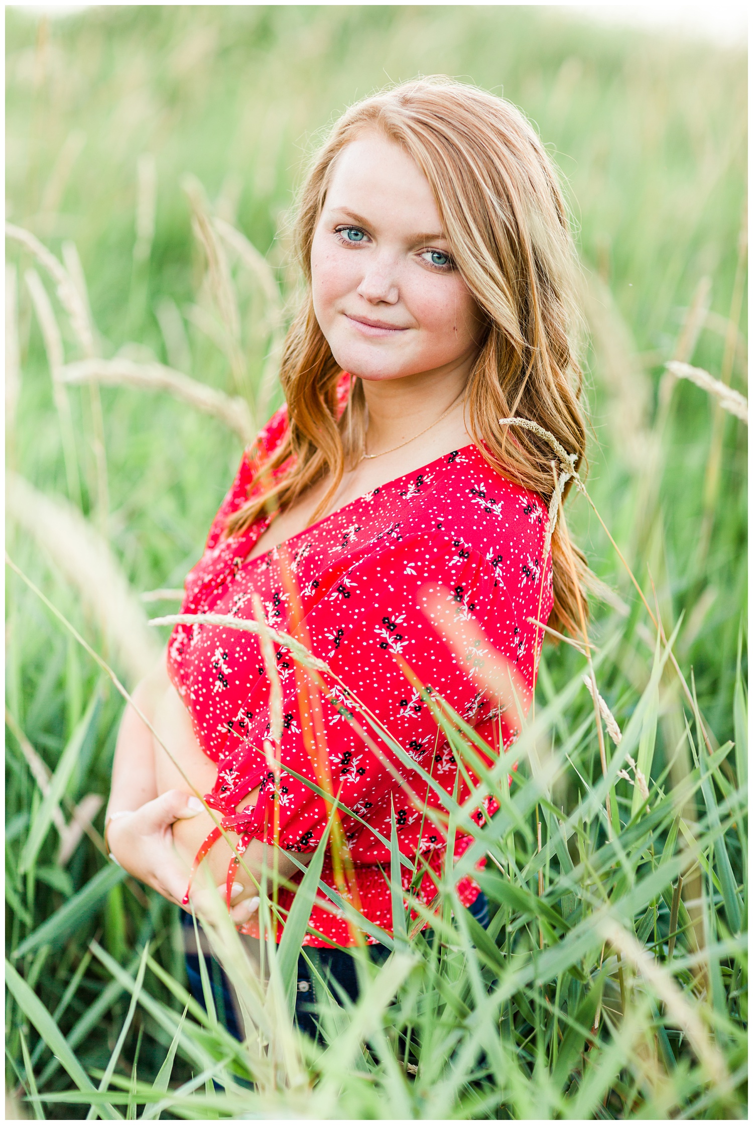 Senior girl wearing a red floral blouse standing in a grassy field at Smith Lake, Algona, Iowa | CB Studio