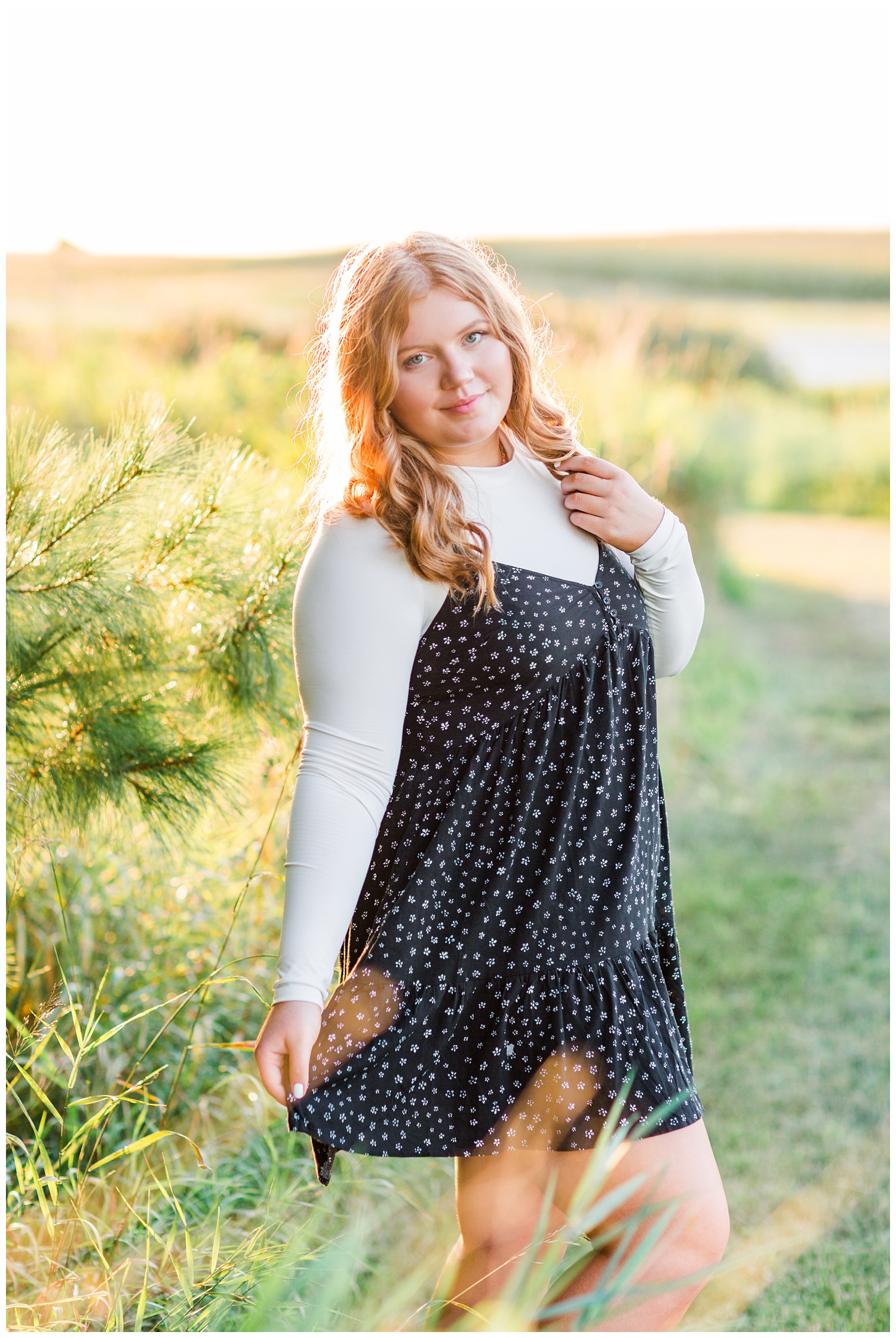 Senior girl wearing a black floral dress stands in a yellow flower field at Water's Edge Nature Center in Algona, Iowa | CB Studio