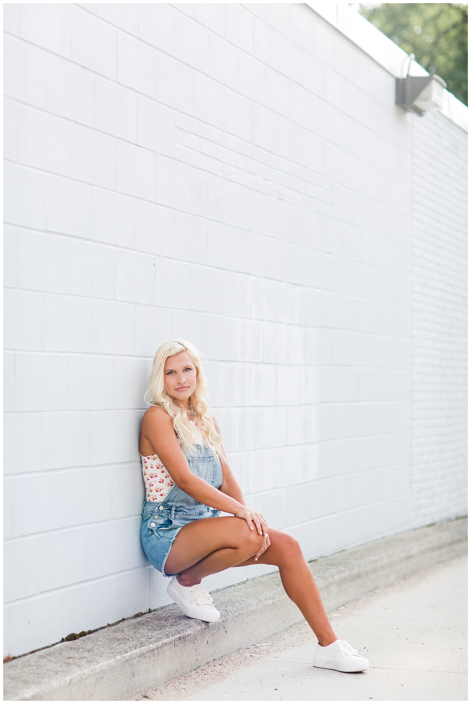 Senior girl sits up against a sky blue brick wall in downtown Algona, Iowa | CB Studio