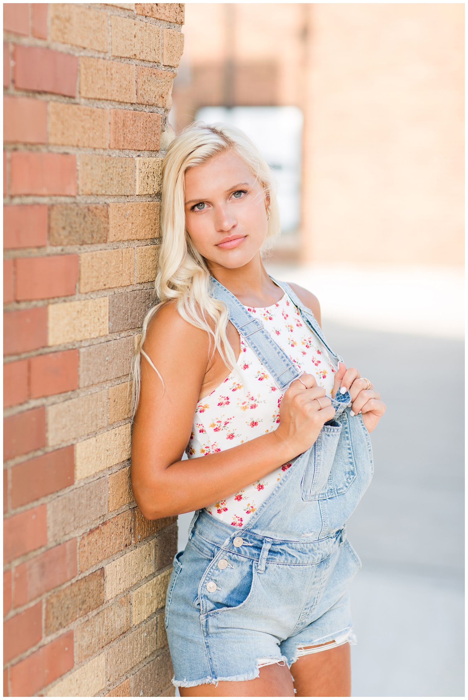 Senior girl wearing overalls leans against a brick wall in downtown Algona, Iowa | CB Studio