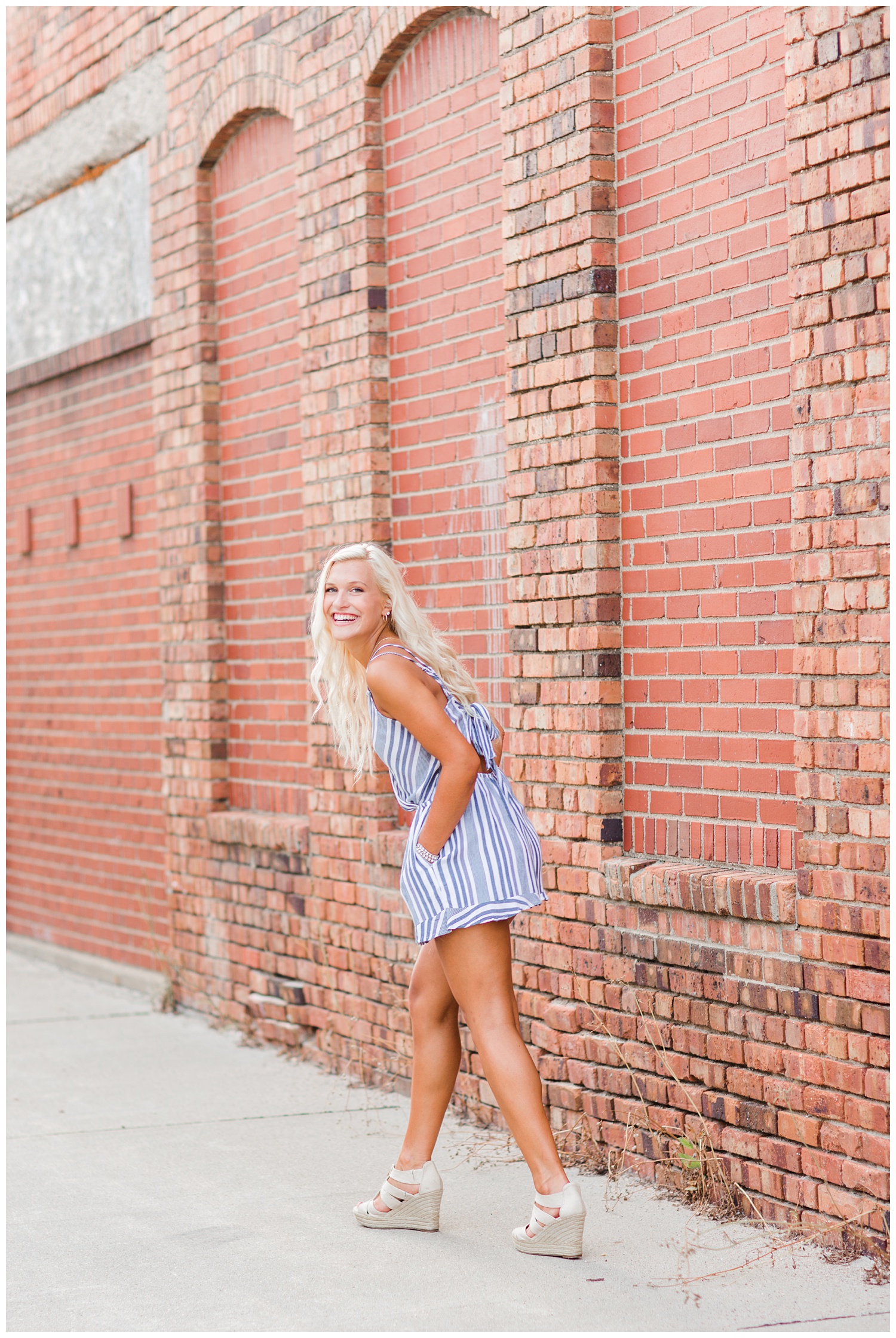 Senior girl wearing a white and blue romper laughs while walking down an alley way in downtown Algona, Iowa | CB Studio