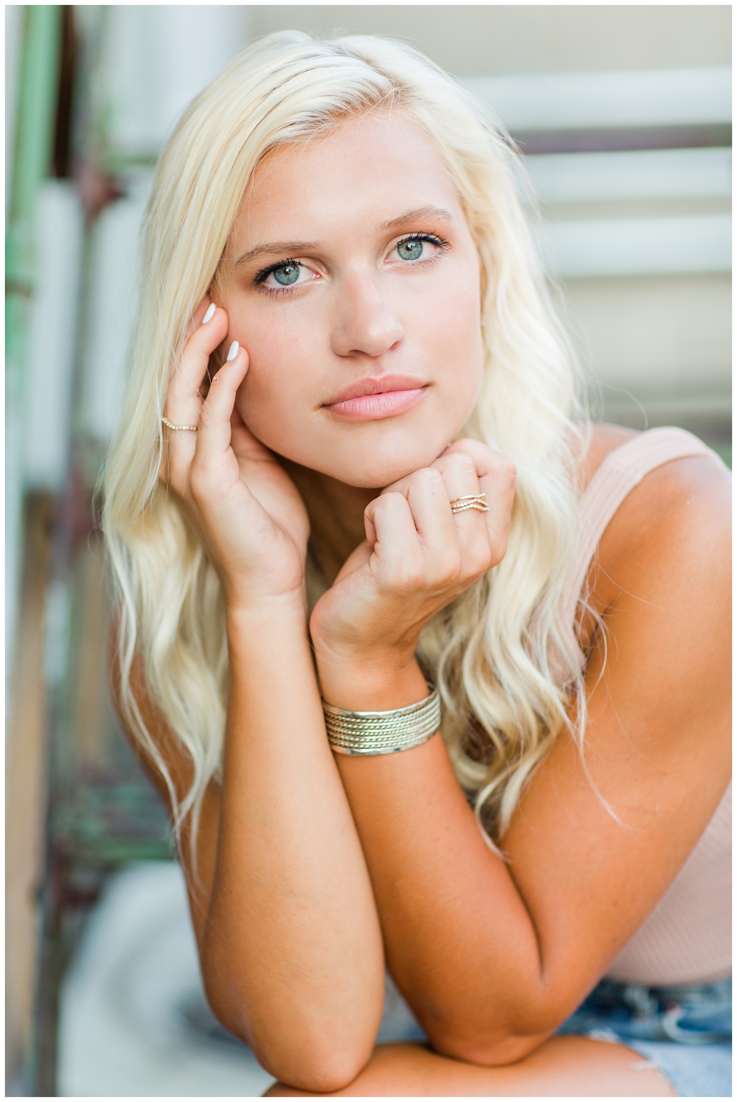 Senior girl cups her hands around her face while siting on a rusty metal staircase in downtown Algona, Iowa | CB Studio