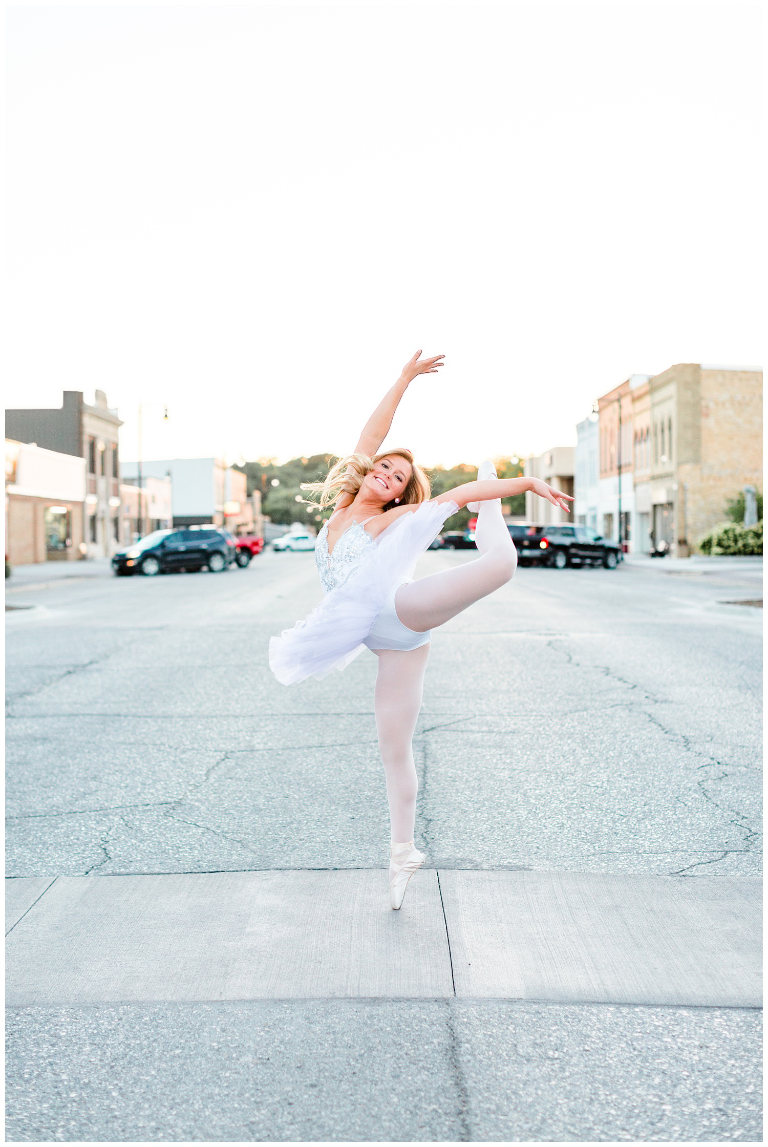 Senior dance photography girl performs an arabesque in full classical ballet white tutu in the middle of Sumner Ave in downtown Humboldt, Iowa | CB Studio