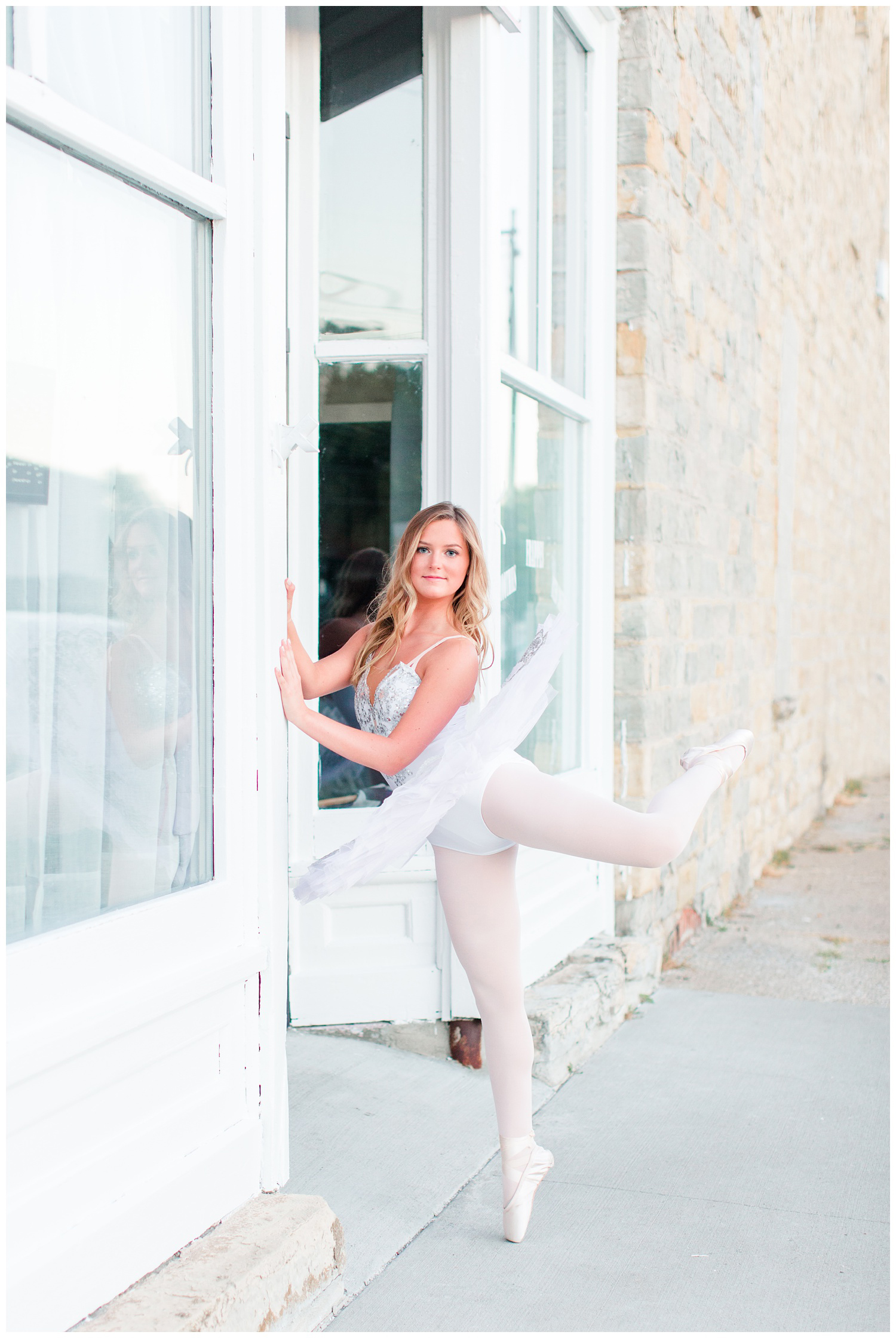 Senior dance photography girl performs a derriere attitude in full classical ballet white tutu in downtown Humboldt, Iowa | CB Studio