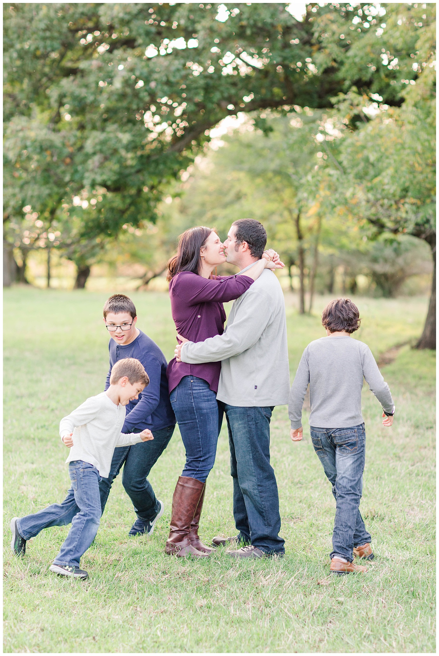 Mom and dad hug close for a kiss while the boys run around them in circles in a pasture in rural Iowa | CB Studio