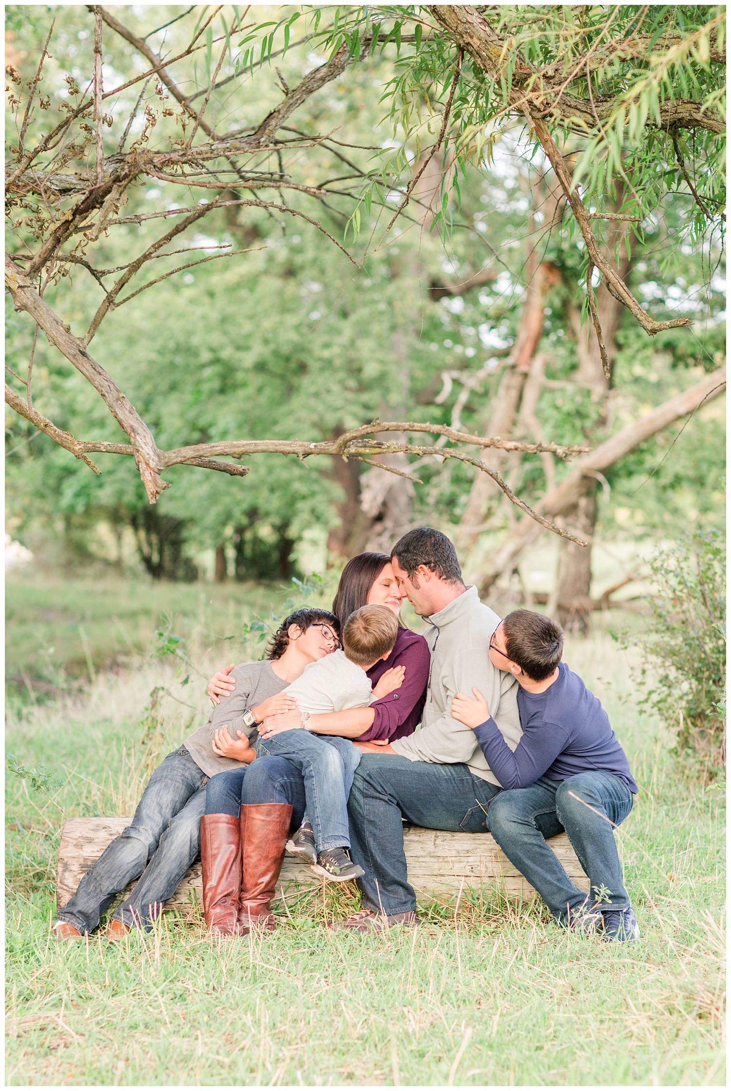 Family snuggles in close while sitting on a log in a pasture in rural Iowa | CB Studio