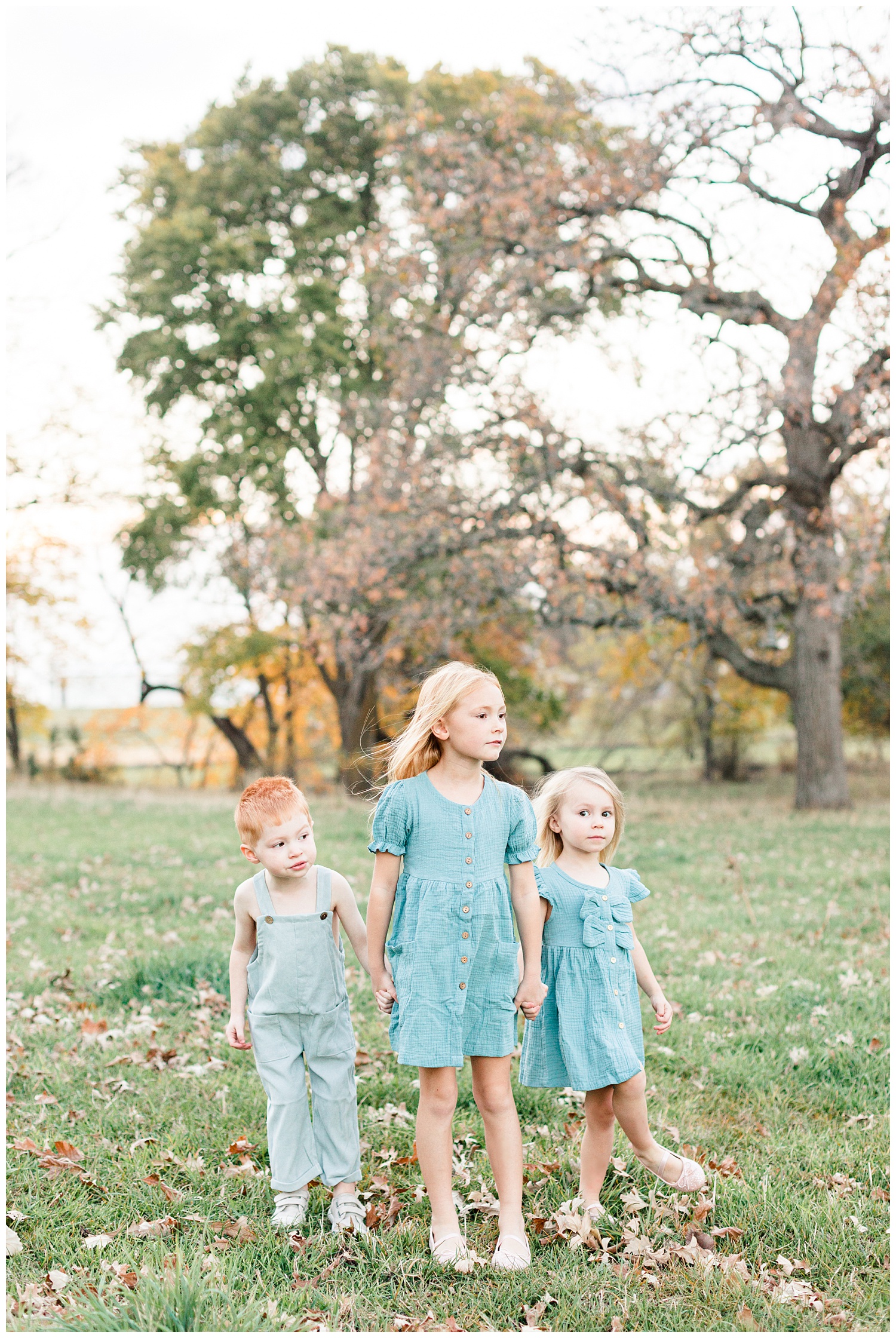 Three children dressed in vintage teal stand holding hands in a grassy field looking onward | CB Studio
