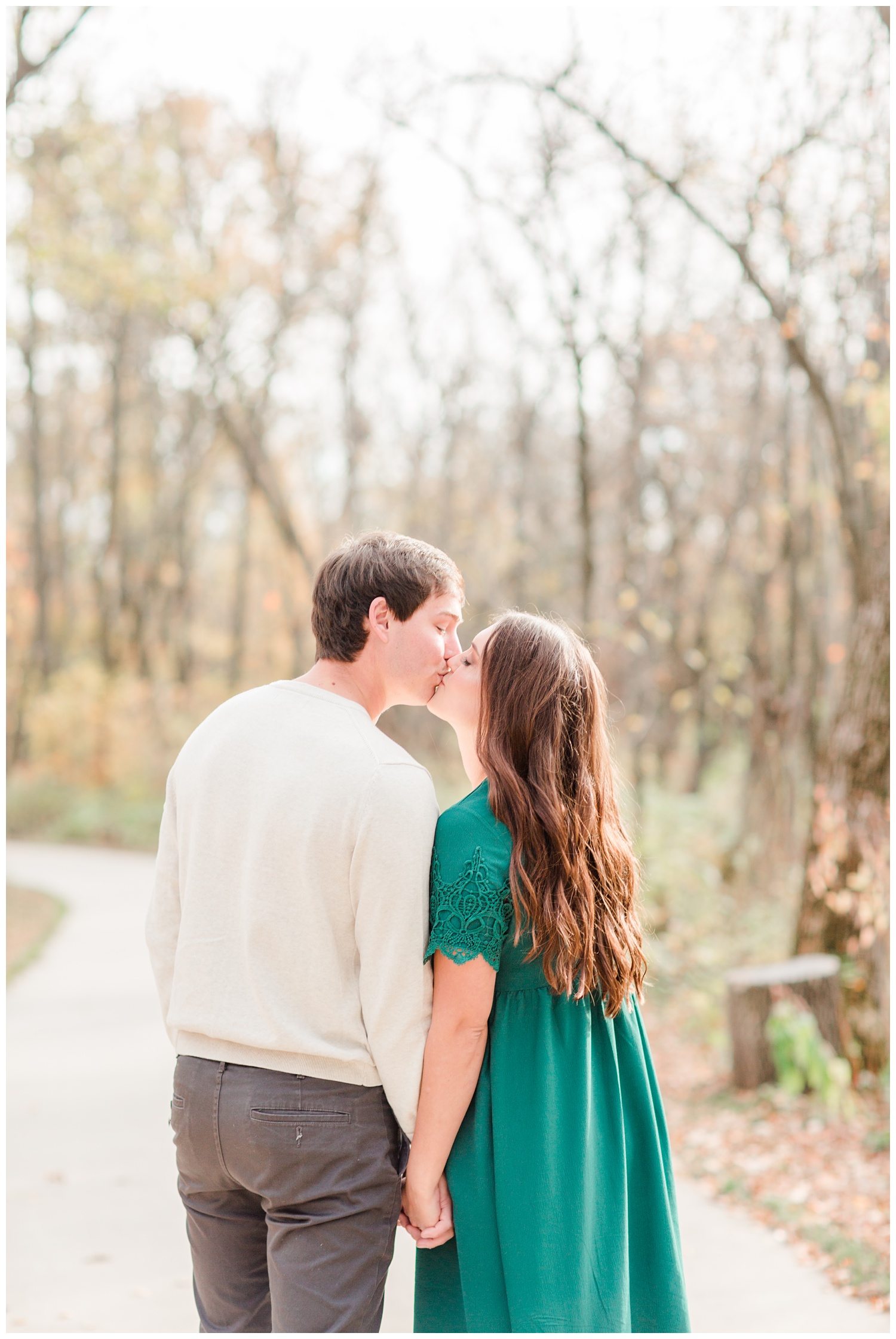 Fall in Iowa, Jenna wearing an emerald green dress kisses Brady in the middle of an autumn path at Lost Island Nature Center | CB Studio