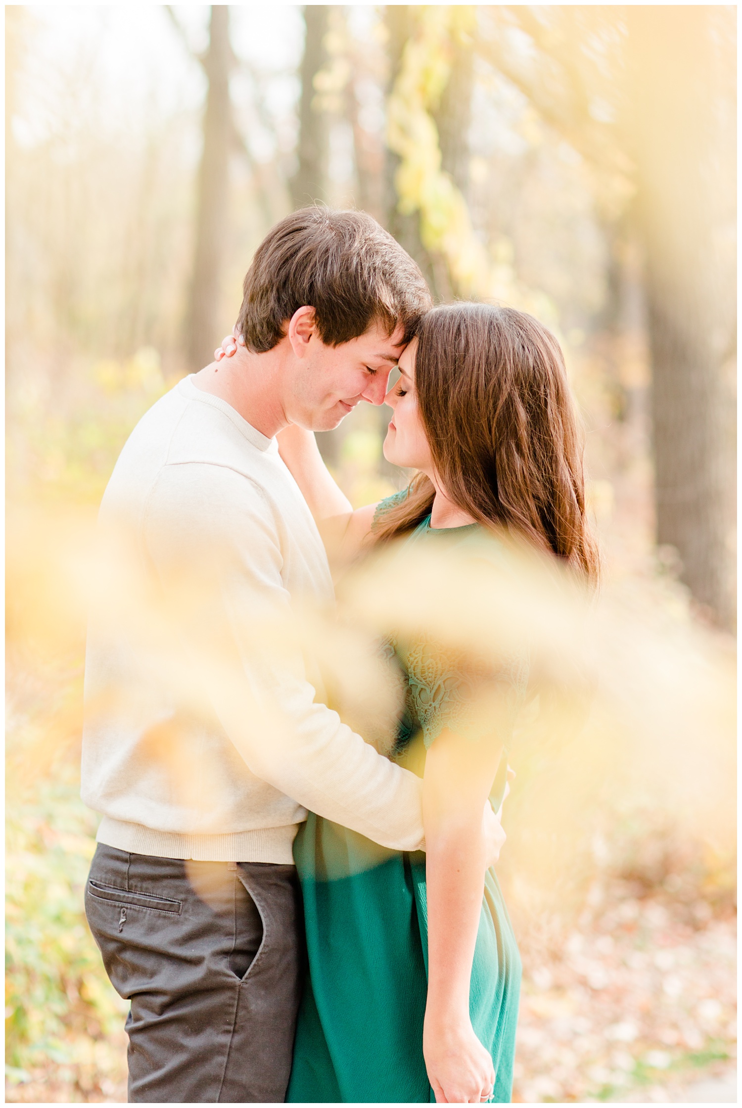 Fall in Iowa, Jenna wearing an emerald green dress embraces Brady in the middle of an autumn path at Lost Island Nature Center | CB Studio